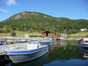 Hafenidylle bei Hitra, Norwegen: Boote liegen im klaren Wasser vor malerischen Holzhütten und bewaldeten Hügeln. Perfekte Kulisse für einen Angelurlaub mit traumhaften Bedingungen und reicher Natur. Ideal für Abenteuer und Erholung.