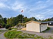 Hölzerne Hütte in der malerischen Landschaft von Hitra, Norwegen, umgeben von grünen Bäumen. Eine norwegische Flagge weht im Wind, idealer Ort für Angelurlaub und Naturliebhaber. Perfekter Rückzugsort für Erholung und Abenteuer.