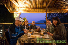 Gemütliche Abendstimmung in Hälsingland, Schweden: Gruppe genießt gemeinsames Abendessen auf überdachter Terrasse mit Blick auf malerische Landschaft bei Dämmerung. Perfekt für Angelreisende, die Natur und kulinarische Genüsse verbinden möchten.