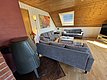 Ein gemütliches Wohnzimmer in Hitra, Norwegen, mit Holzdach, grauen Sofas, Kamin und einem großen Fenster, das viel Tageslicht bietet. Ideal für entspannte Abende nach einem erfolgreichen Angeltrip.
