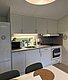 Kompakte, moderne Küche in Hitra, Norwegen, mit heller Einrichtung und Fensterblick. Ausgestattet mit Spüle, Ofen, Mikrowelle, Kühlschrank und Kaffeemaschine – ideal für Angelreisende. Gemütlicher Essbereich für gesellige Mahlzeiten nach einem erfolgreichen Fischtag.