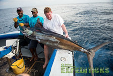 Angler posieren mit beeindruckendem Fang, einem großen Fisch, auf einem Boot vor den Malediven. Ideal für Angelreisen, zeigt das Bild Abenteuerlust und Erfolg beim Meeresangeln. Perfektes Reiseziel für passionierte Angler.