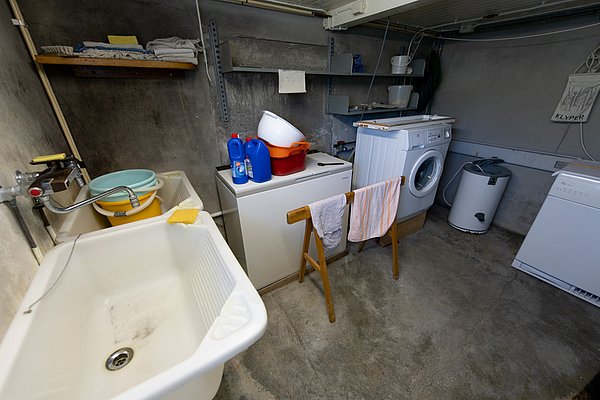 Waschküche in Nordland, Norwegen: Betonboden, Waschmaschine, Spülbecken, Reinigungsmittel, hölzernes Trockengestell. Funktionaler Raum für Hausarbeiten in rustikaler Umgebung. Praktisch und kompakt gestaltet für effiziente Nutzung.