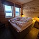Gemütliches Schlafzimmer in einer skandinavischen Hütte mit Holzwänden. Großes Fenster bietet Blick auf die schneebedeckte Landschaft Nord-Norwegens. Ideal für erholsamen Angelurlaub und Abenteuer in der Natur.