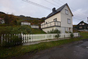 Traditionelles weißes Holzhaus in Nord-Norwegen, umgeben von grüner Landschaft und Bergen. Ein typisches ländliches Setting, ideal für Natur- und Angelreisen in Norwegen. Entspannung und Abenteuer in skandinavischer Umgebung.