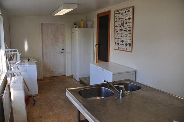 Heller Raum in Nordland, Norwegen mit Küchenspüle, weißen Gefrierschränken und Fischposter. Praktischer Ort zum Reinigen und Lagern von Fängen nach einem erfolgreichen Angeltag in spektakulärer Umgebung.