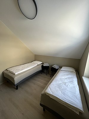 Ein gemütliches Schlafzimmer in Nordland, Norwegen, mit zwei Einzelbetten, Holzboden und minimalistischer Einrichtung, ideal für Erholung und Entspannung nach einem langen Angeltag. Perfekt für Angelreisende.