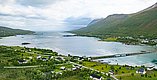 Luftaufnahme einer idyllischen Küstenlandschaft in Nord-Norwegen. Ein ruhiger Fjord umgeben von sattgrünen Bergen und verstreuten Häusern. Ideal für Angelabenteuer und Naturliebhaber. Über eine Brücke gelangt man in die unberührte Natur.