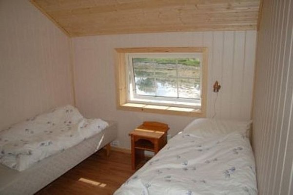 Gemütliches Schlafzimmer in einer Holzhütte in Nordland, Norwegen, mit zwei Einzelbetten, Holzmöbeln und einem Fenster mit Ausblick auf die ruhige, grüne Umgebung. Perfekt für Entspannungs- und Angelurlaub.