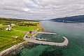 Luftaufnahme einer idyllischen Küstenlandschaft in Nord-Norwegen mit grünem Land, farbigen Häusern und ruhigem, klaren Wasser. Perfekter Ort für Angelreisen und Naturerkundungen in skandinavischer Umgebung.
