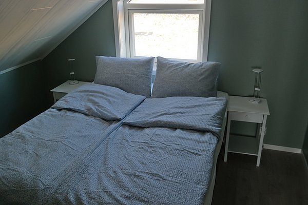 Gemütliches Schlafzimmer in Nordland, Norwegen, mit einem Doppelbett, weißen Nachttischen und natürlichem Licht durch das Fenster. Perfekt für erholsame Nächte auf deiner Angelreise.