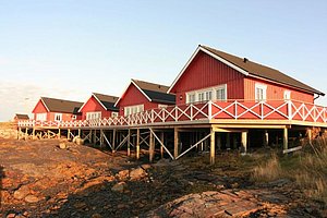 Rote Holzhäuser auf Stelzen am felsigen Ufer in Nordland, Norwegen. Perfekter Ort für Angelreisen, umgeben von atemberaubender Natur. Ideal zum Meeresangeln und entspannen. Skandinavische Idylle und Abenteuerstimmung vereint.