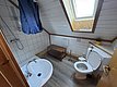 Helles Badezimmer in Hitra, Norwegen mit Dachfenster, weißer Holzverkleidung und blauen Duschvorhängen. Ausstattung: Dusche, WC, Waschbecken und Holzregal. Ideal für Angelurlaub mit Komfort.