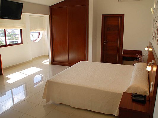 Ein helles, minimalistisches Schlafzimmer mit einem großen Bett, einem Flachbildfernseher, Holzmöbeln und einem runden Fenster mit Tageslicht. Ein helles, minimalistisches Schlafzimmer mit einem großen Bett, einem Flachbildfernseher, Holzmöbeln und einem runden Fenster mit Tageslicht.