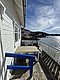 Weißes Holzhaus mit Terrasse am Wasser, blauer Himmel, perfekte Angelkulisse in Hitra, Norwegen. Ideal für erholsamen Angelurlaub in skandinavischer Umgebung. Entspanntes Ambiente lädt zum Fischen und Entdecken ein.