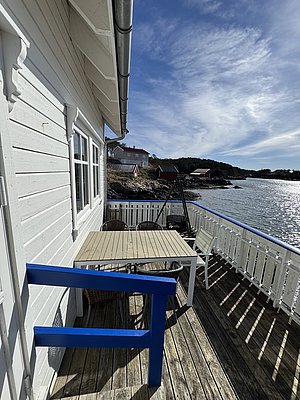Weißes Holzhaus mit Terrasse am Wasser, blauer Himmel, perfekte Angelkulisse in Hitra, Norwegen. Ideal für erholsamen Angelurlaub in skandinavischer Umgebung. Entspanntes Ambiente lädt zum Fischen und Entdecken ein.