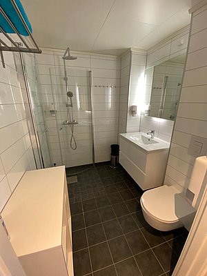 Modernes Badezimmer in Nord-Norwegen: Helle Fliesen, Glasdusche, weißer Waschtisch und dunkler Boden. Komfortable Ausstattung in stilvollem skandinavischen Design für entspannenden Angelurlaub.