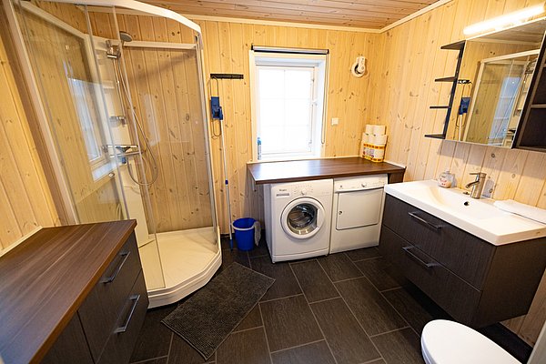 Badezimmer in Nordland, Norwegen: Holzwände, Dusche, Waschbecken, Waschmaschine, Trockner und moderne Ausstattung. Ideal für Angler, die Komfort nach dem Angelabenteuer suchen. Entspanntes Ambiente in natürlicher Umgebung.