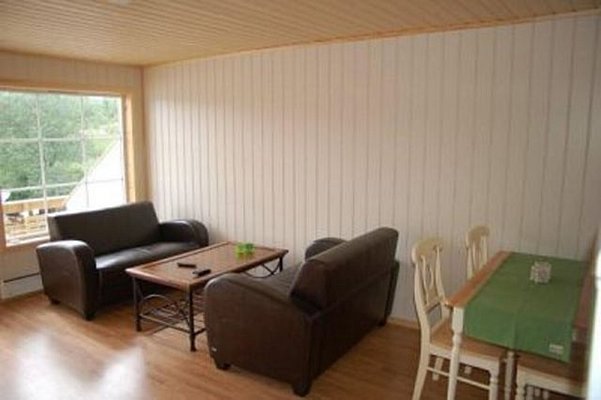 Gemütliches Wohnzimmer in Nordland, Norwegen: Holzboden, Leder-Sofas, Couchtisch und Esstisch mit grüner Tischdecke. Große Fenster bieten Ausblick auf die Natur. Ideal für erholsame Angelreisen und entspannte Abende.