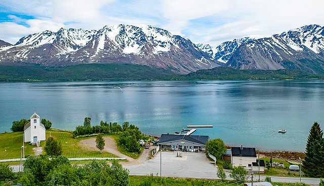 Klares blaues Wasser, schneebedeckte Berge und ein malerisches Dorf prägen die atemberaubende Landschaft von Nord-Norwegen. Perfekter Ort für Angelreisen und Naturerlebnisse, um neue Abenteuer zu entdecken.