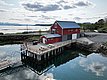 Rote Fischerhütte am fjordnahen Steg in Nord-Norwegen. Ruhiges Wasser, reflektierender Himmel und malerische Landschaft im Hintergrund. Ideal für Angelreisen und Outdoor-Abenteuer in Skandinavien.