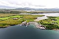 Luftaufnahme der idyllischen Küstenlandschaft in Nordland, Norwegen: grüne Wiesen, kleiner Bootshafen und beeindruckende Fjorde. Ideal für Angelreisen, Abenteuer und Erholung in malerischer Umgebung. Perfekter Ausgangspunkt für unvergessliche Angelabenteuer.