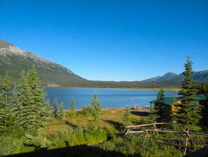 Kluane Lake im Yukon, Kanada: Ein klarer Bergsee umgeben von grünen Tannen und majestätischen Bergen, unter strahlend blauem Himmel. Perfektes Ziel für Naturliebhaber und Angelbegeisterte. Ideal zum Entdecken unberührter Wildnis und Ruhe.
