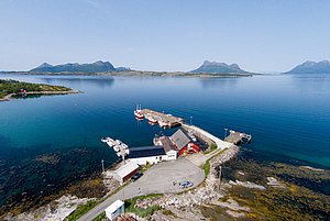 Luftaufnahme von einem malerischen kleinen Hafen in Nordland, Norwegen. Klare blaue Gewässer, umgeben von Bergen und idyllischen Gebäuden, ideal für Angelurlaube und Meeresangeln. Perfekter Ort für Naturliebhaber und Abenteurer.