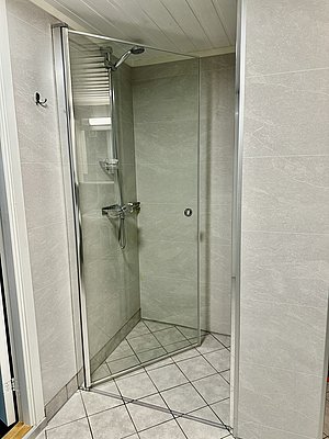 Moderne Dusche in einer Unterkunft in Nord-Norwegen mit grauen Fliesen und Glastür, ideal für Angelreisende, die Komfort und Entspannung nach einem erfolgreichen Angeltag suchen.