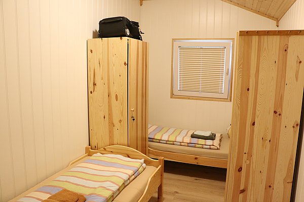 Gemütliches Schlafzimmer in Norwegens Hitra, mit zwei Einzelbetten, Holzschrank und Fenster. Helle, einladende Atmosphäre für Angeltouren. Perfekte Unterkunft für Erholung nach aufregenden Abenteuern in der Umgebung. Ideal für Angelurlaub in Norwegen.