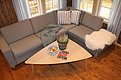 Gemütliches Wohnzimmer in Nordnorwegen mit grauem Ecksofa, Holztisch, Früchteschale und Dekoaccessoires. Ideal für Entspannung nach einem erfolgreichen Angelurlaub. Helle Fenster bieten Blick auf norwegische Landschaft.
