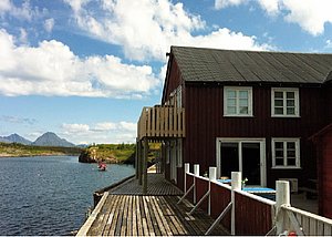 Rotes Holzhaus am Fjord in Nordland, Norwegen. Malerische Landschaft mit Bergen und blauem Himmel. Ideal für Angelreisen und Naturliebhaber. Perfekter Ausgangspunkt für Erholung und Abenteuer im hohen Norden.