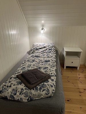 Gemütliches Einzelzimmer in Nord-Norwegen mit hellem Holzinterieur, Bett mit gemusterter Bettdecke und Nachttisch, ideal für erholsame Nächte während Ihres Angelurlaubs. Perfekt für Entspannung nach einem erfolgreichen Angeltag.