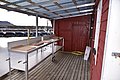 Überdachter Filetierplatz am Wasser in Südwest-Norwegen, ideal für Angler. Rote Holzwände, robuste Arbeitsflächen mit Schneidebrettern und Schläuchen. Perfekt für den Angelurlaub und Frischfisch-Vorbereitung. Abenteuerliche Küstenumgebung.