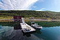 Klarer Fjord in Nord-Norwegen mit rotem Ferienhaus am Steg und Booten. Üppige grüne Hügel bilden die idyllische Kulisse. Perfekter Ausgangspunkt für einen unvergesslichen Angelurlaub.
