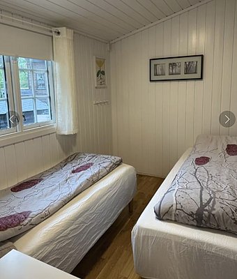 Gemütliches Schlafzimmer in einer Hütte nahe Hitra, Norwegen. Zwei Einzelbetten mit Naturbettwäsche, helle Holzwände und ein Fenster mit Ausblick. Perfekt für Angelreisende auf der Suche nach erholsamer Ruhe und skandinavischer Gemütlichkeit.