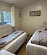 Gemütliches Schlafzimmer in einer Hütte nahe Hitra, Norwegen. Zwei Einzelbetten mit Naturbettwäsche, helle Holzwände und ein Fenster mit Ausblick. Perfekt für Angelreisende auf der Suche nach erholsamer Ruhe und skandinavischer Gemütlichkeit.