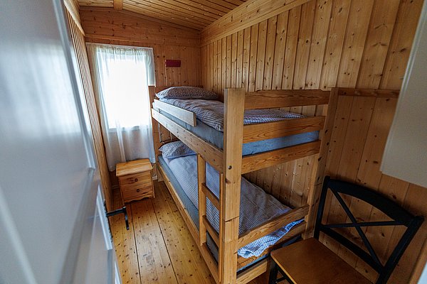 Gemütliches Holzzimmer mit Etagenbett, heller Einrichtung und Fenster mit Vorhängen. Ländliches Flair in Hitra, Norwegen, ideal für Angler auf Entdeckungstour. Perfekter Rückzugsort nach einem erlebnisreichen Angeltag.