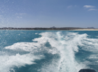 Klares, türkisblaues Meer in São Vicente, Kapverden. Bootsspur zieht sich durch das Wasser, weite Küstenlandschaft und sanfte Hügel im Hintergrund unter strahlend blauem Himmel. Ideal für Angelabenteuer und Erkundungen.