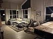 Gemütliches, modernes Wohnzimmer einer Angelhütte in Hitra, Norwegen. Große Fenster, Ecksofa, Holztisch und angenehme Beleuchtung schaffen eine einladende Atmosphäre für Reisende und Angelurlauber. Perfekt für Entspannung nach einem erfolgreichen Angeltag.