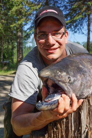 Ein Angler hält stolz seinen beeindruckenden Fang, einen großen Lachs, in der Region Lake Creek, Alaska. Perfekter Ort für Angelreisen, umgeben von malerischer Natur und reichen Fangchancen. Ideal für Abenteuerlustige.