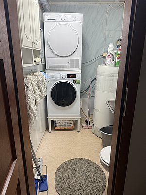 Waschraum in Nord-Norwegen: Moderne Waschmaschine und Trockner, nahegelegene Reinigungsmittel und Korb für Wäsche. Praktische Einrichtung für täglichen Komfort. Ideal für Reisende nach Outdoor-Abenteuern und Angelreisen in Norwegen.