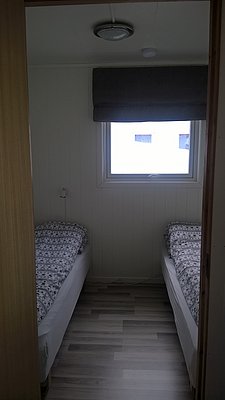 Gemütliches Schlafzimmer in Nord-Norwegen mit zwei Einzelbetten, hellem Holzfußboden und Fenster für Tageslicht. Ideal für Anglerurlaub und entspannte Nächte nach einem aufregenden Angelausflug in der traumhaften skandinavischen Landschaft.