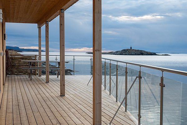 Moderne Terrasse mit Glasgeländer in Hitra, Norwegen, bietet weiten Blick aufs Meer und eine kleine Insel. Ideal für Angelreisen und Naturerlebnisse in skandinavischer Ruhe. Perfekter Ausgangspunkt für Meeresangeln und Erholung.