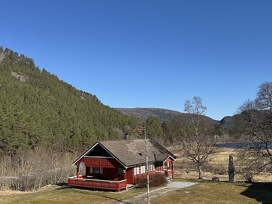 Rotes Holzhaus in malerischer Landschaft von Hitra, Norwegen. Umgeben von dichten Wäldern, Bergen und klarem Himmel. Ideal für Angelurlaube und Naturgenuss in skandinavischer Idylle. Perfekter Ausgangspunkt für Abenteurer und Erholungssuchende.