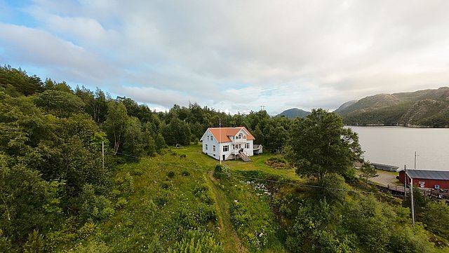 Landschaft in Hitra, Norwegen: Ein weißes Haus mit rotem Dach inmitten grüner Wälder und mit Blick auf einen ruhigen Fjord, ideal für Angelurlaub und Naturerlebnisse. Perfekt für Abenteuer und Entspannung in der skandinavischen Wildnis.
