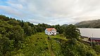 Landschaft in Hitra, Norwegen: Ein weißes Haus mit rotem Dach inmitten grüner Wälder und mit Blick auf einen ruhigen Fjord, ideal für Angelurlaub und Naturerlebnisse. Perfekt für Abenteuer und Entspannung in der skandinavischen Wildnis.