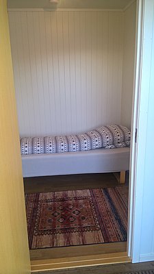 Gemütliches, kleines Schlafzimmer in Nord-Norwegen mit Einzelbett, traditionellem Teppich und hellem Holzinterieur. Ideal für Angelurlauber, die Entspannung und Abenteuer kombinieren möchten. Perfekte Basis für Erkundungen und Angelerlebnisse in Skandinaviens Naturparadies.
