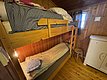 Gemütliche Holzhütte in Hitra, Norwegen: Stapelbett mit karierten Bettdecken, Holzwände und -boden, kleines Fenster mit Vorhängen. Perfekt für einen entspannten Angelurlaub in skandinavischem Ambiente.