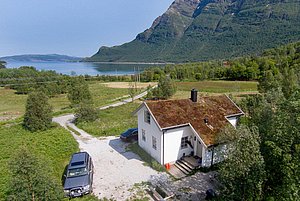 Gemütliches Haus mit Grasdach in Nordland, Norwegen, umgeben von üppiger Natur und beeindruckenden Bergen, mit Blick auf einen ruhigen Fjord. Perfekt für Erholung und Angelabenteuer in atemberaubender Szenerie.
